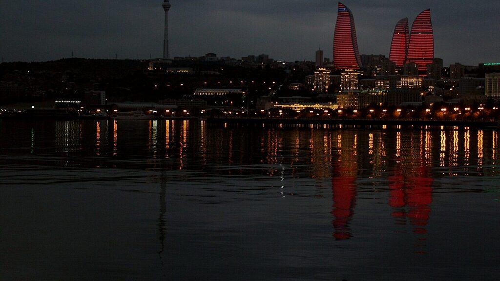 Baku at dusk from the seafront boulevard, the Flame Towers lit red above the city and reflected in the Caspian